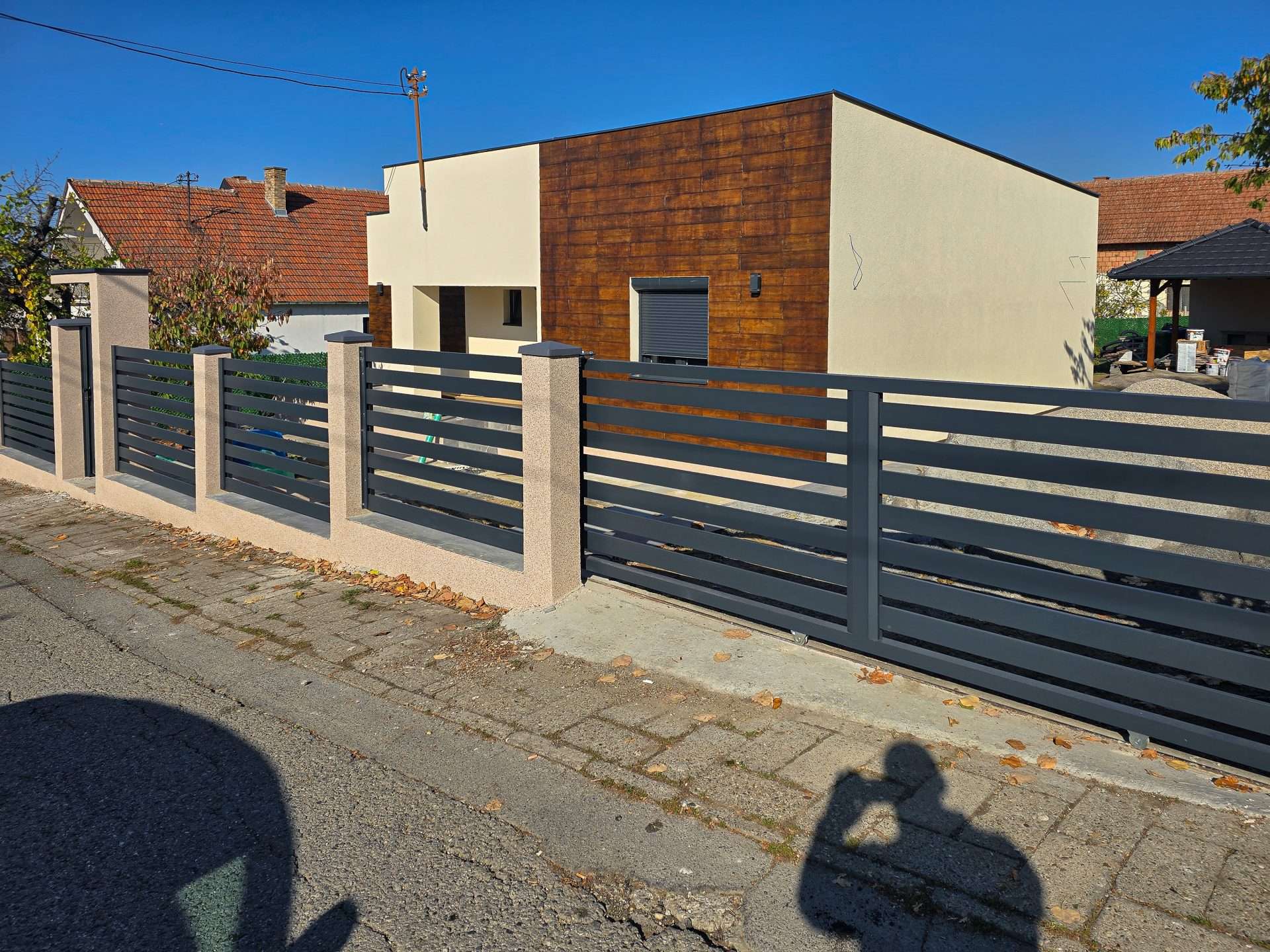 Niska siva aluminijumska ograda sa horizontalnim lamelama ispred male kuće sa drvenom fasadom